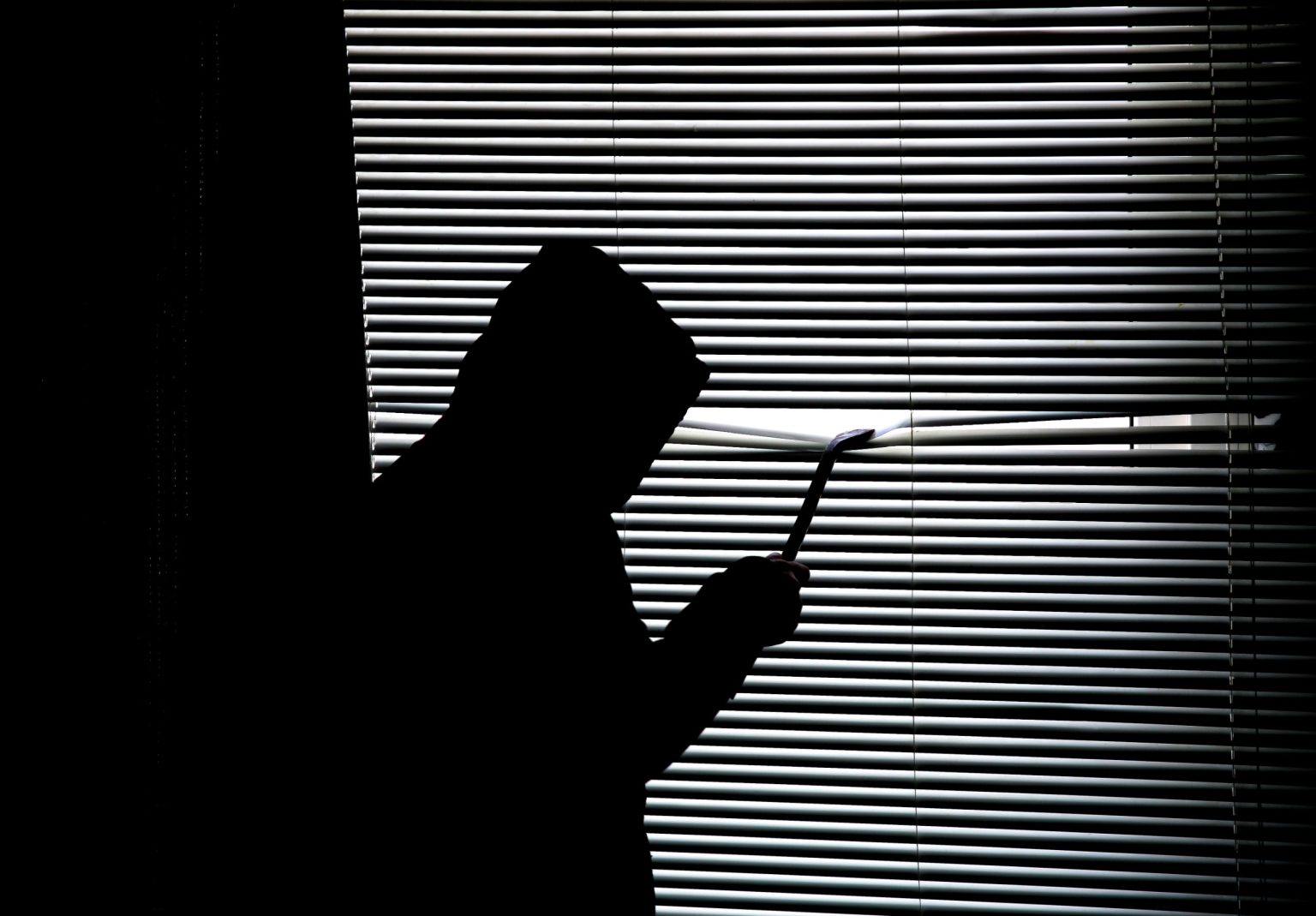 Silhouette encapuchonnée qui force des stores avec un pied-de-biche
